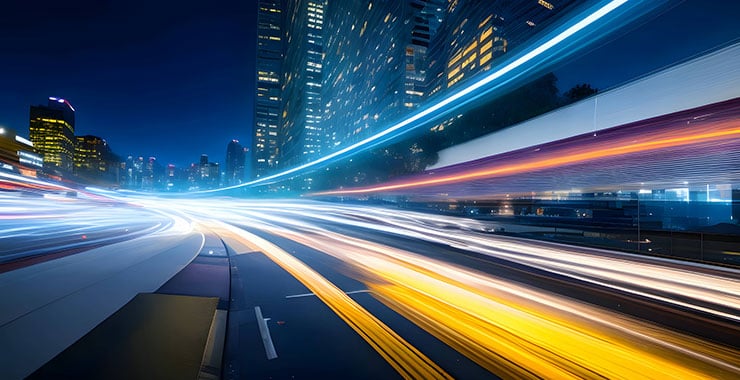 A vibrant city street at night illuminated by colorful light trails from passing vehicles