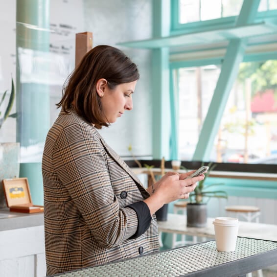 A woman at a cafe, looking at her phone while connecting with a client