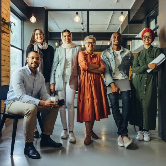 A diverse group of smiling professionals standing together in an office posing for the camera