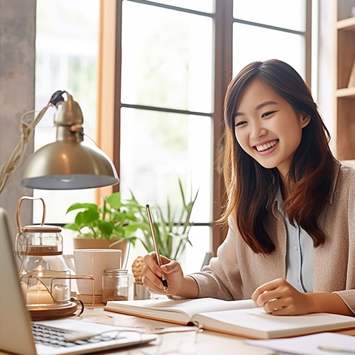 A cheerful woman sits at her desk engaged with her laptop and focus in her workspace