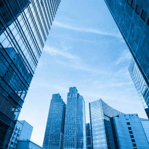 A view looking up at modern office buildings towering against the sky in a bustling cityscape