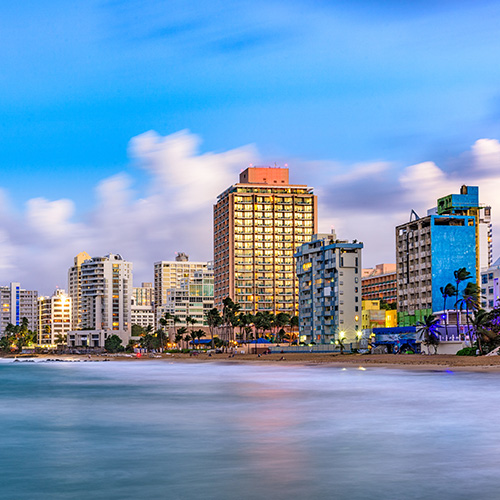 Puerto Rico skyline at sunset with tall buildings, a beach, and the ocean in the foreground