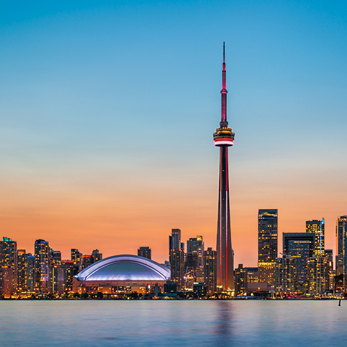 The iconic CN Tower illuminated against a vibrant sunset, with the Toronto skyline and waterfront visible in the background