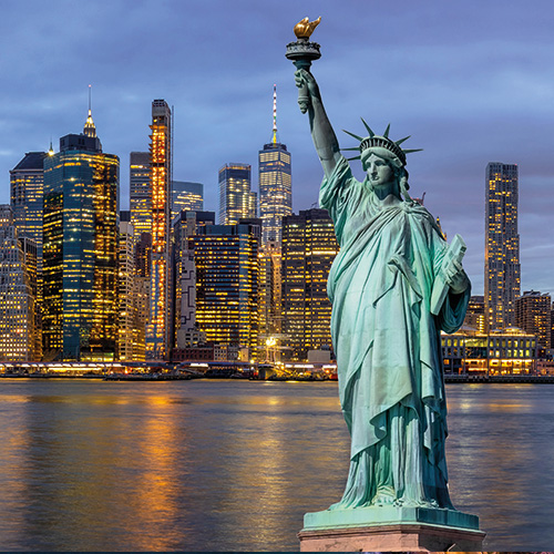 The Statue of Liberty at dusk, with the illuminated Manhattan skyline in the background