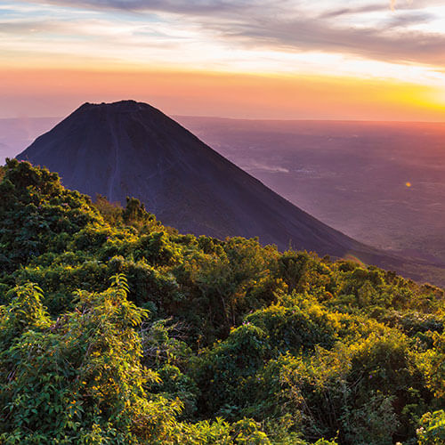 The majestic Izalco Volcano in El Salvador at sunset, with a vibrant sky and lush green forest in the foreground