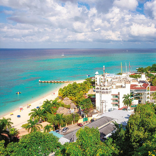 A view of a beautiful white sandy beach and a resort with a pool overlooking the ocean at Montego Bay Jamaica