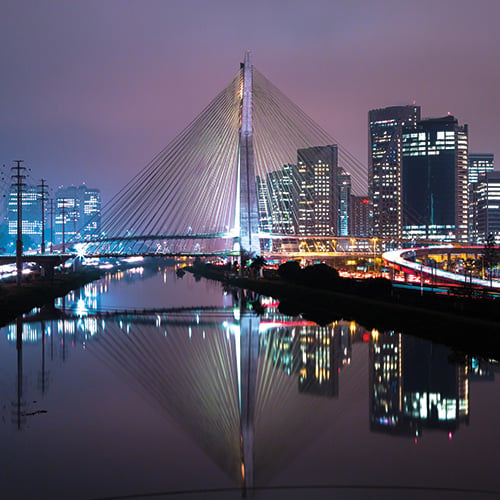 The Estaiada Bridge illuminated at night, with the São Paulo skyline reflected in the water below