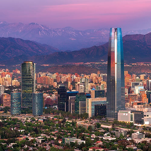 The Gran Torre Santiago skyscraper at dusk with the Andes Mountains and the city of Santiago in the background