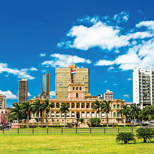 A scenic view of The Palacio de López in Asunción, Paraguay, with a Paraguayan flag flying and lush green lawns in the foreground