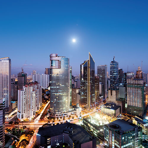 A shot of Makati city, Philippines skyline at night with illuminated skyscrapers and a full moon in the sky