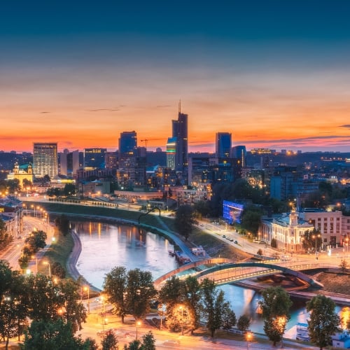 Vilnius, Lithuania city skyline at sunset featuring the Neris River, modern skyscrapers, historic architecture, illuminated bridges, and urban cityscape