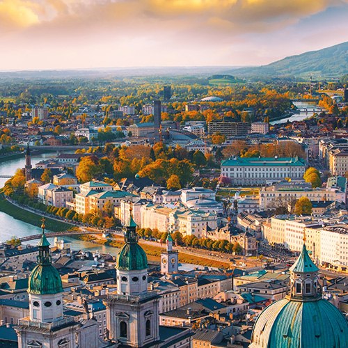 A sunset view of Salzburg, Austria, with the Salzach River winding through the city and mountains in the background