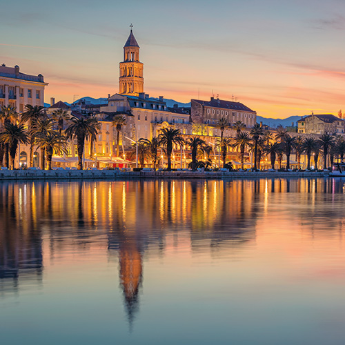 A scenic view of Diocletian's Palace in Split, Croatia, illuminated at sunset with the harbor and waterfront