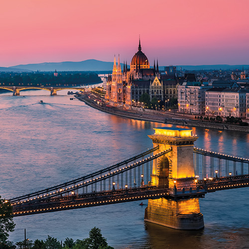 A panoramic view of Budapest, Hungary, at sunset with the Hungarian Parliament Building, Chain Bridge, and Danube River