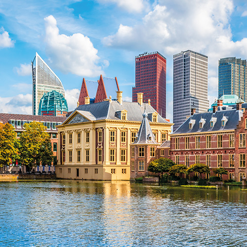 A scenic view of The Hague, Netherlands, showing a mix of historic buildings and modern skyscrapers along the Hofvijver lake