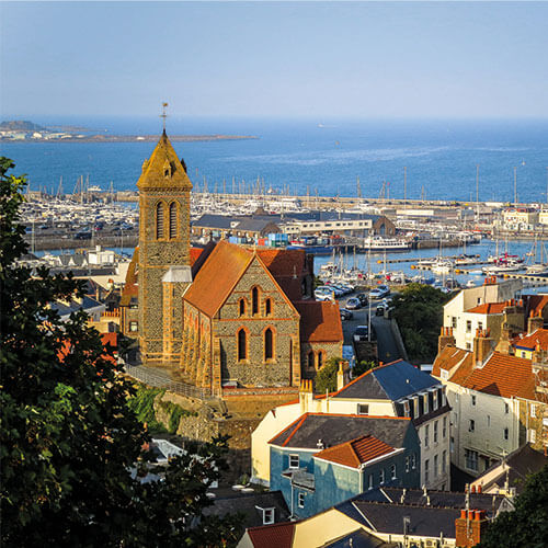 A panoramic view of St. Peter Port, Guernsey, showing a historic church and a bustling harbor with sailboats