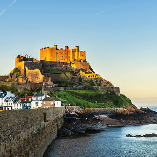 An aerial view of Mont Orgueil Castle, a medieval castle perched on a rocky headland overlooking the sea in Jersey