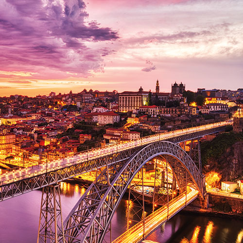 A panoramic view of Porto, Portugal, at sunset, featuring the Dom Luís I Bridge illuminated over the Douro River