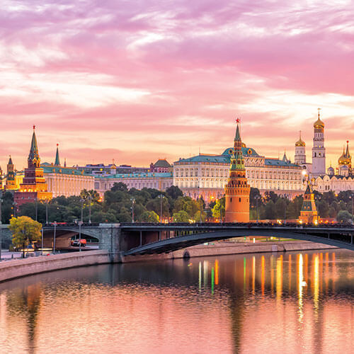 A scenic view of Moscow, Russia, at sunset, featuring the Kremlin, St. Basil's Cathedral, and the Moskva River