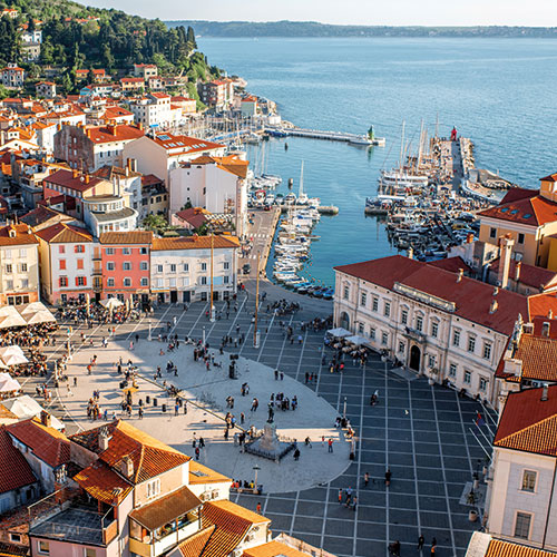 An aerial view of Piran, Slovenia, showing the colorful houses, the central square, and the harbor with boats