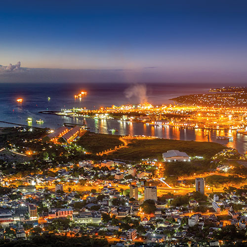 A panoramic view of Port Louis, Mauritius, at night, showing the city lights, the harbor, and the surrounding coastline