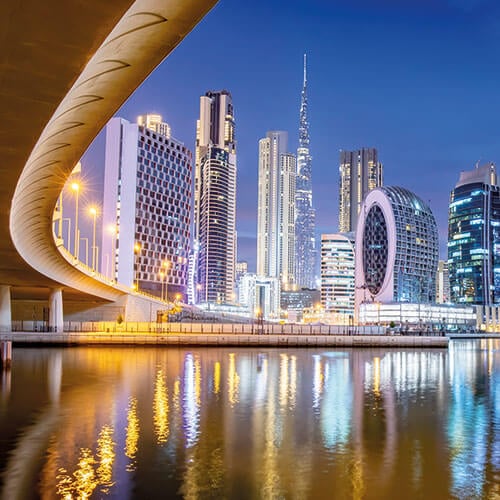 A stunning night shot of Dubai's skyline, featuring the iconic Burj Khalifa and other skyscrapers reflected in the calm waters of the Dubai Water Canal