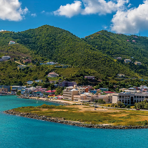 A scenic view of the Road Town, Tortola, with colorful buildings lining the waterfront and hills in the background