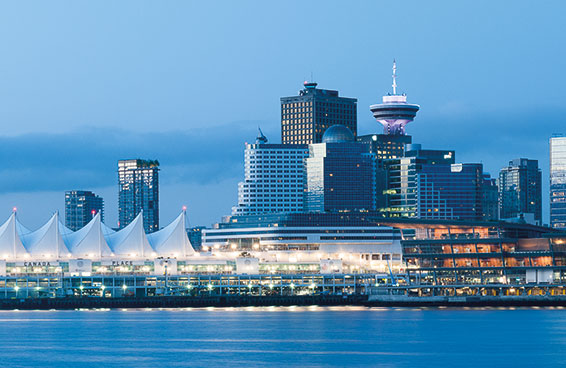 A panoramic view of the Vancouver skyline at dusk, with the distinctive sails of Canada Place and the iconic CN Tower