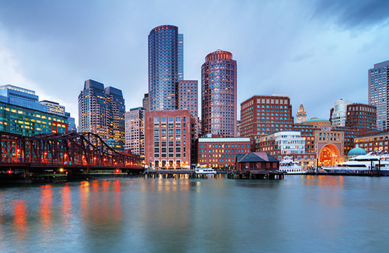 An aerial view of the Boston skyline at dusk, with the Financial District and a bridge over the water