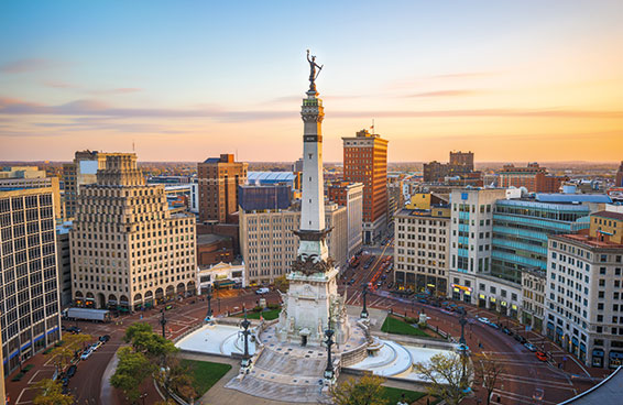 A panoramic view of the Monument Circle in Indianapolis, Indiana, at sunset, with the Soldiers & Sailors Monument and surrounding buildings