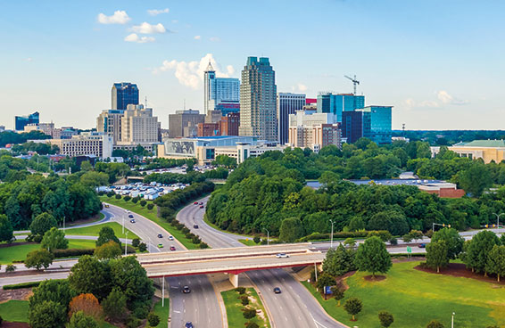 A panoramic view of Raleigh skyline with a highway and green spaces in the foreground