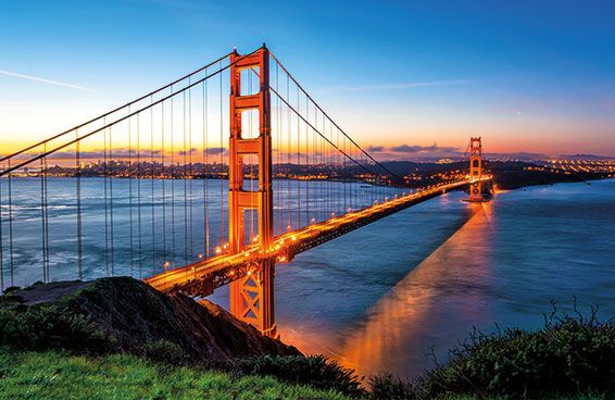 An aerial view of the Golden Gate Bridge at sunset, with the city skyline visible in the background