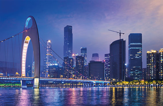 A shot of Guangzhou skyline at dusk with lit skyscrapers, a suspension bridge, and river reflections