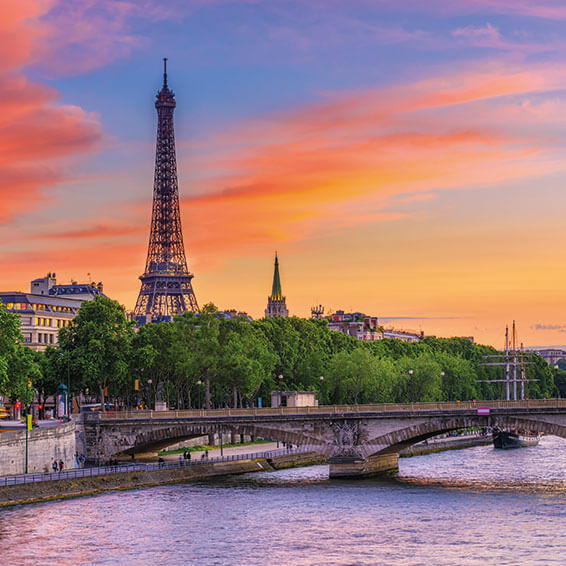 A panoramic view of the Eiffel Tower at sunset, with the Seine River and a bridge in the foreground