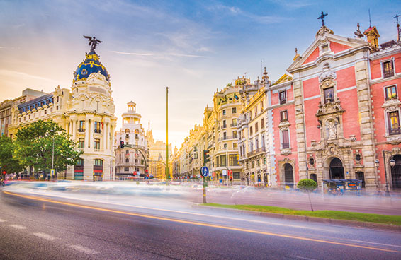 A vibrant photo of Gran Via in Madrid at dusk, with the Metropolis Building and other iconic buildings