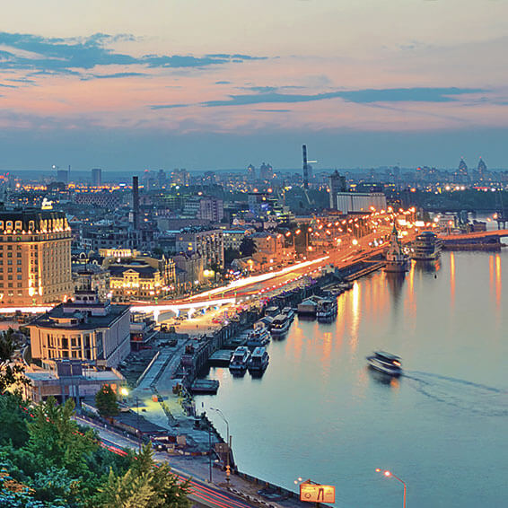 A view of Kyiv at dusk, with the Dnieper River, the Podil district, and the Kyiv Pechersk Lavra in the background