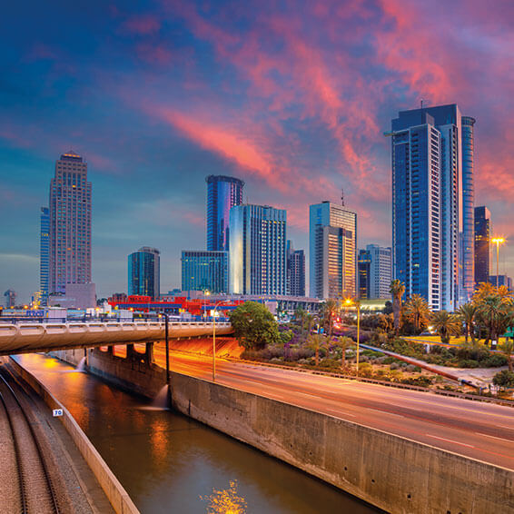 A cityscape of Tel Aviv, Israel, at dusk, with the Yarkon River in the foreground and a vibrant skyline in the background