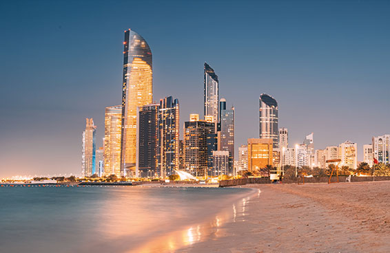 A view of the Abu Dhabi skyline at night, with the iconic Etihad Towers illuminated along the Corniche beach