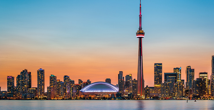 A panoramic view of the iconic CN Tower illuminated against a vibrant sunset, with the Toronto skyline and waterfront