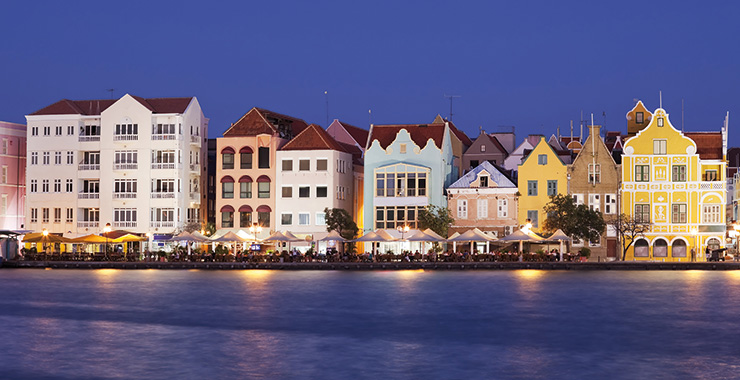 A panoramic view of the colorful buildings lining the waterfront in Willemstad, Curaçao, at dusk