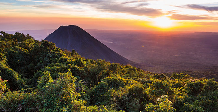 A scenic view of the majestic Izalco Volcano in El Salvador at sunset, with a vibrant sky and lush green vegetation