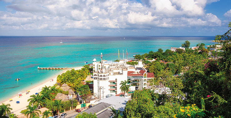 A view of a beautiful white sandy beach and a resort with a pool overlooking the ocean at Montego Bay Jamaica