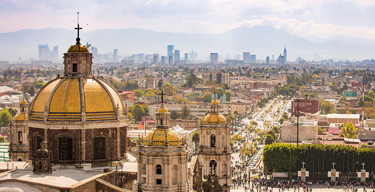 A stunning night shot of the Basilica of Our Lady of Guadalupe in Mexico City with its golden domes and the bustling city skyline in the background