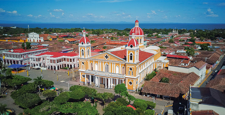 Aerial view of the Granada Cathedral in Nicaragua, with its iconic orange and red facade, surrounded by colonial-style buildings and Lake Nicaragua