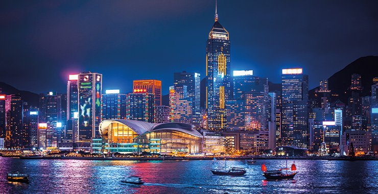 A panoramic view of Hong Kong skyline at night with illuminated skyscrapers and boats in the harbor