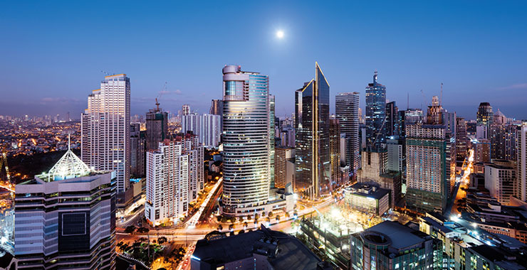 A shot of Makati city, Philippines skyline at night with illuminated skyscrapers and a full moon in the sky