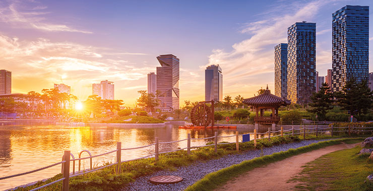 Sunset view of Songdo, South Korea, with modern skyscrapers and a traditional Korean pavilion next to a pond