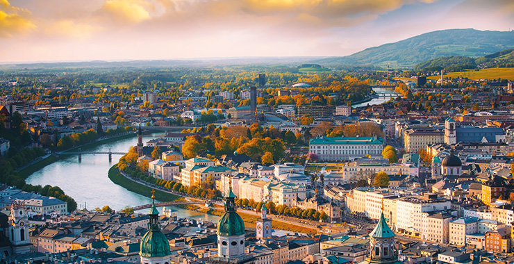 A sunset view of Salzburg, Austria, with the Salzach River winding through the city and mountains in the background