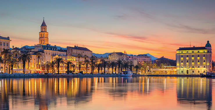 A scenic view of Diocletian's Palace in Split, Croatia, illuminated at sunset with the harbor and waterfront