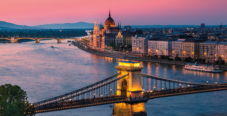 A panoramic view of Budapest, Hungary, at sunset with the Hungarian Parliament Building, Chain Bridge, and Danube River